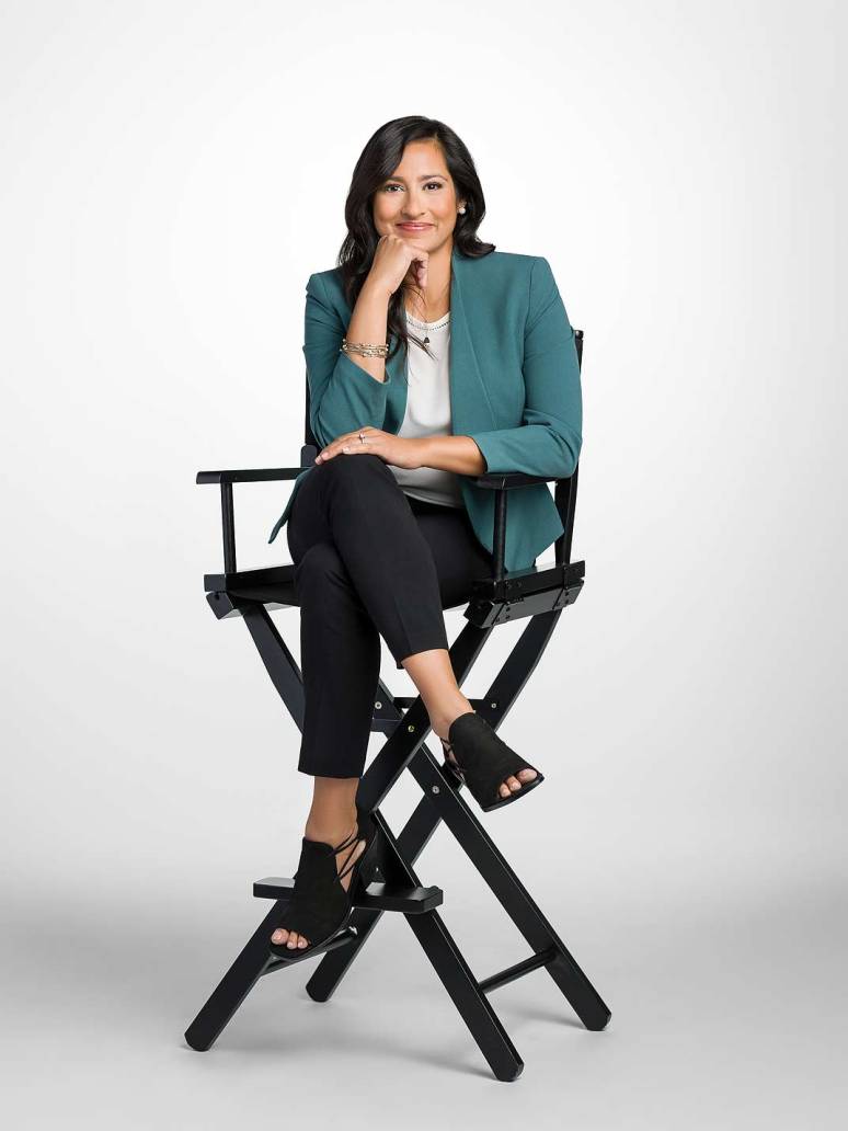 A female attorney sits in a director's chair leaning on her hand looking friendly