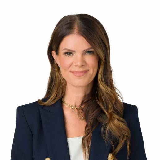 A headshot of a professional looking corporate woman wearing a navy suit smiling at the camera