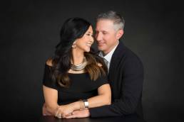 A mature couple dressed for their 25th anniversary embrace smiling and looking at each other