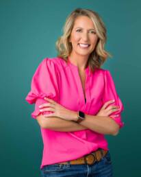 A smiling female photographed in a studio setting standing with her arms folded.