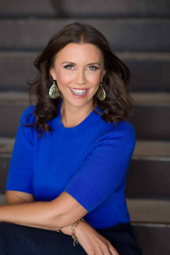 A mid-life woman sitting on an outdoor staircase with the wind in her hair looking happy and loving her life.