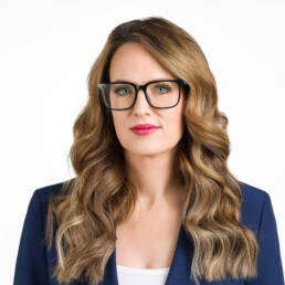 A Denver female CFO wearing glasses and a navy blazer photographed on a white backdrop looking serious and smart.