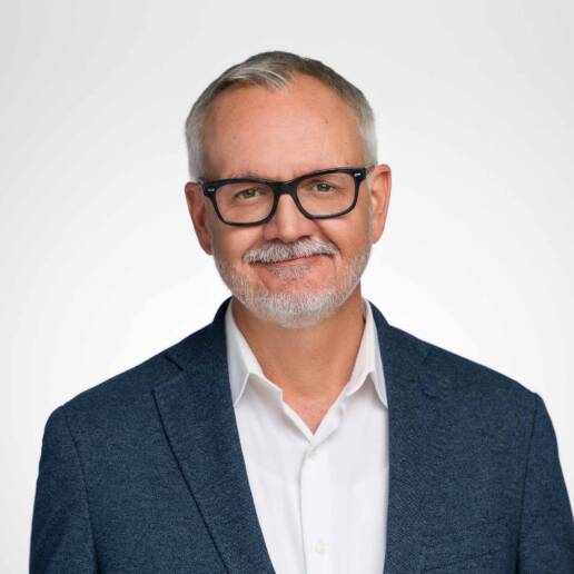 A company headshot of a male photographed on a white background with a closed lip smile.