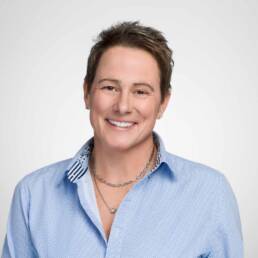 A smiling woman looking at the camera photographed on a white backdrop looking personable and welcoming.