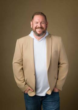 A personal brand portrait of a man wearing a blazer with a hoodie and jeans on a brown background