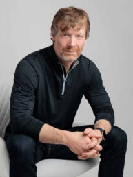 A man sitting on a modern office chair leaning on his forearms with hands together looking calm, confident, and satisfied.