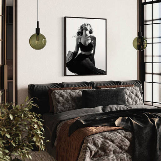 Hung on the wall over a bed sits a black and white beauty portrait in a black frame of a long-haired woman with her head back and skirt flowing in the wind.