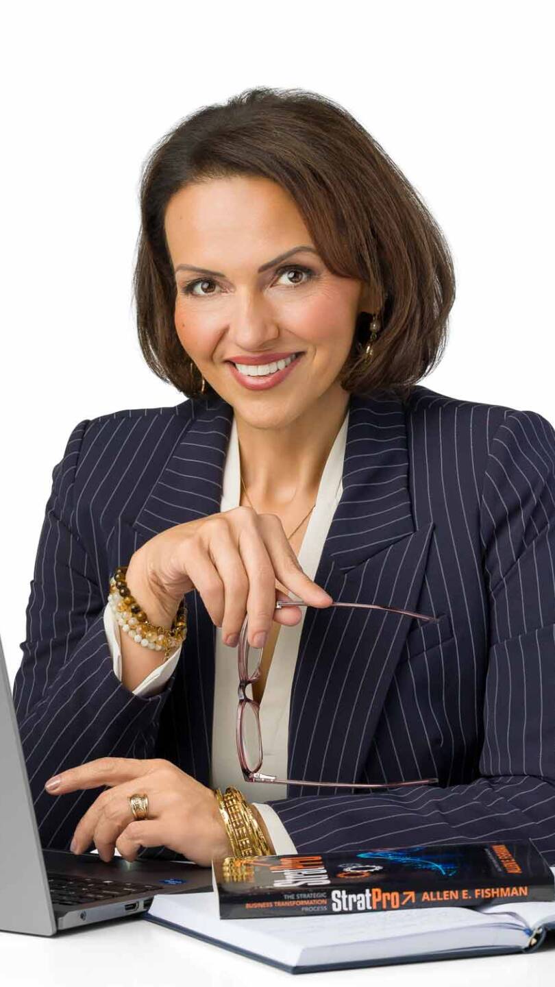 A woman in a pinstripe blazer sits at her computer holding her glasses looking smart and approachable