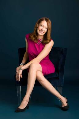 A female Denver financial advisor sits on a navy chair wearing a hot pink dress