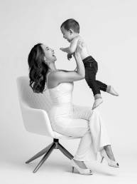 A stylish mother holds her toddler in the air smiling and laughing at each other