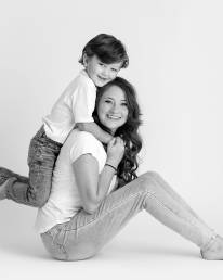 A teen mom wearing jeans and a tshirt sits on the floor with your toddler on her back